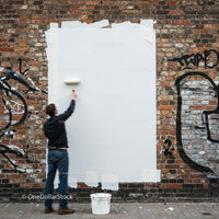 Man Painting Over Graffiti on Urban Brick Wall