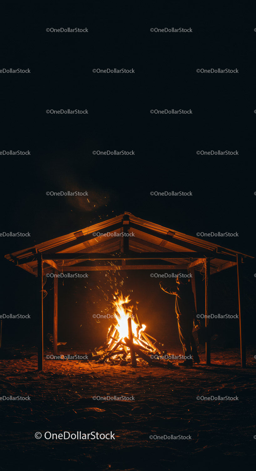 Man warming hands by fire under wooden shelter at night