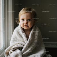 Toddler wrapped in soft blanket by window light