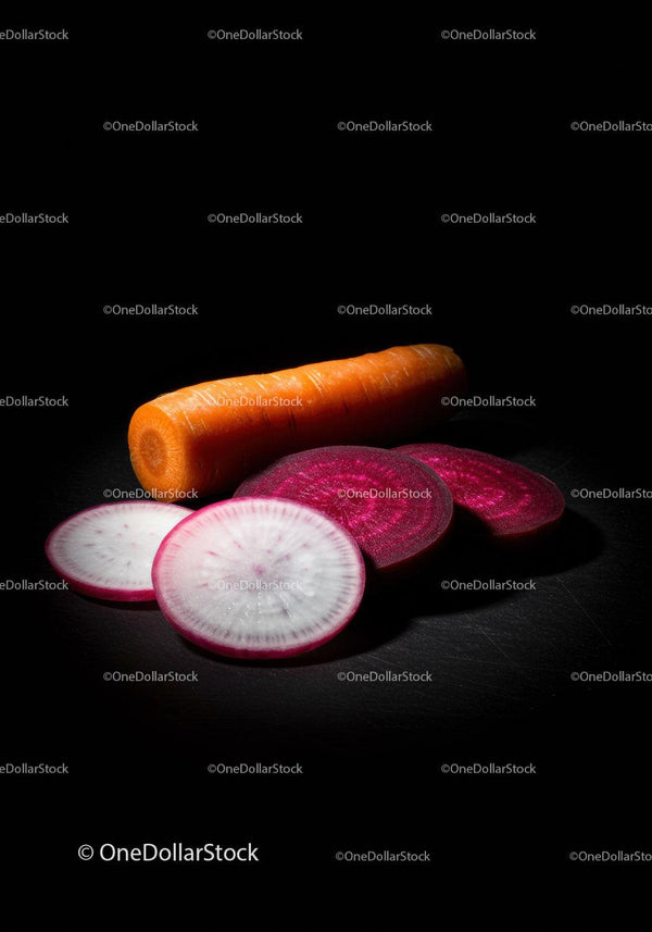 Fresh sliced radishes and whole carrot on dark surface