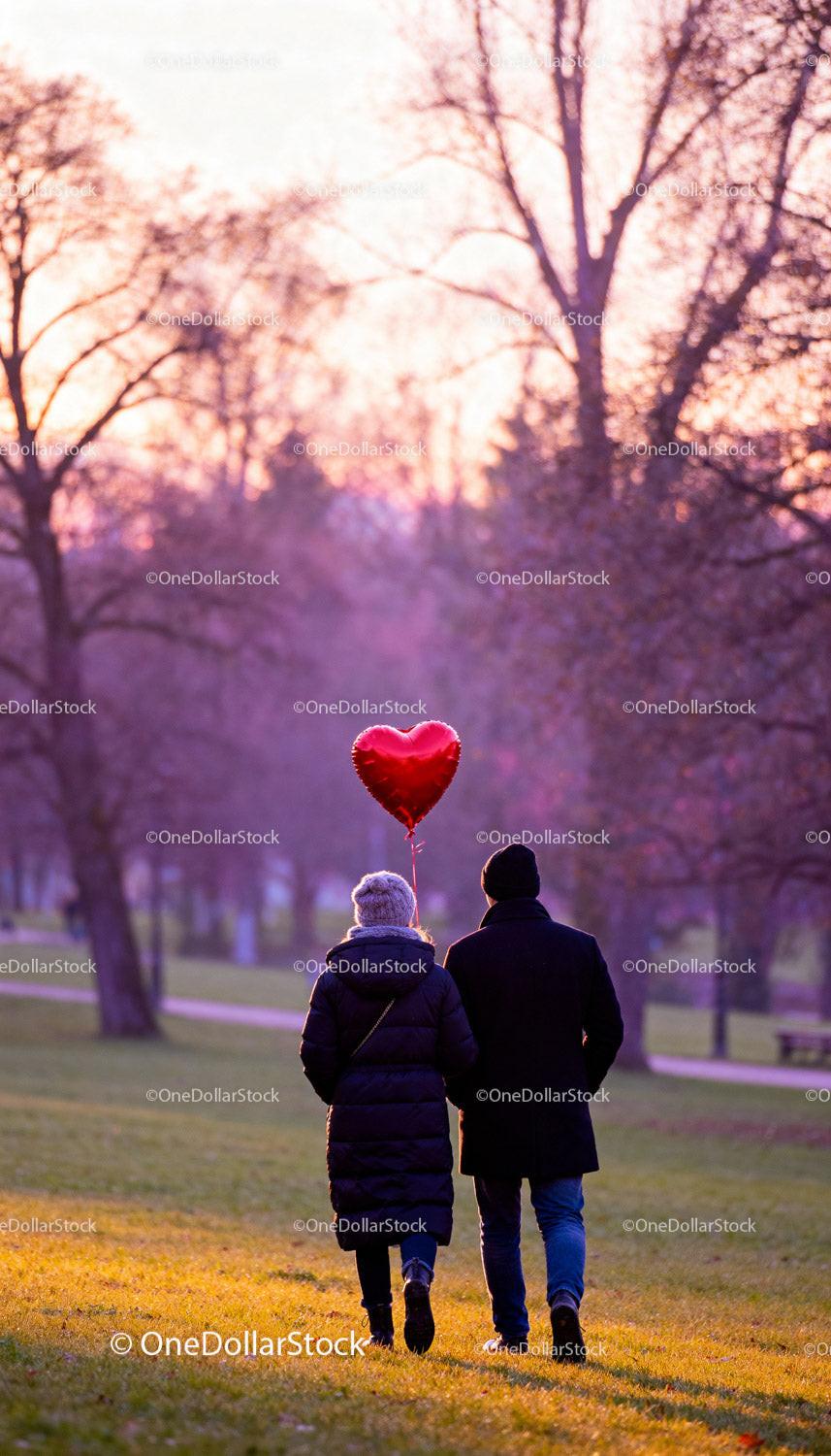 Couple walking in park holding red heart balloon