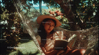 Young Woman Sitting in Hammock Reading Book in Tropical Garden