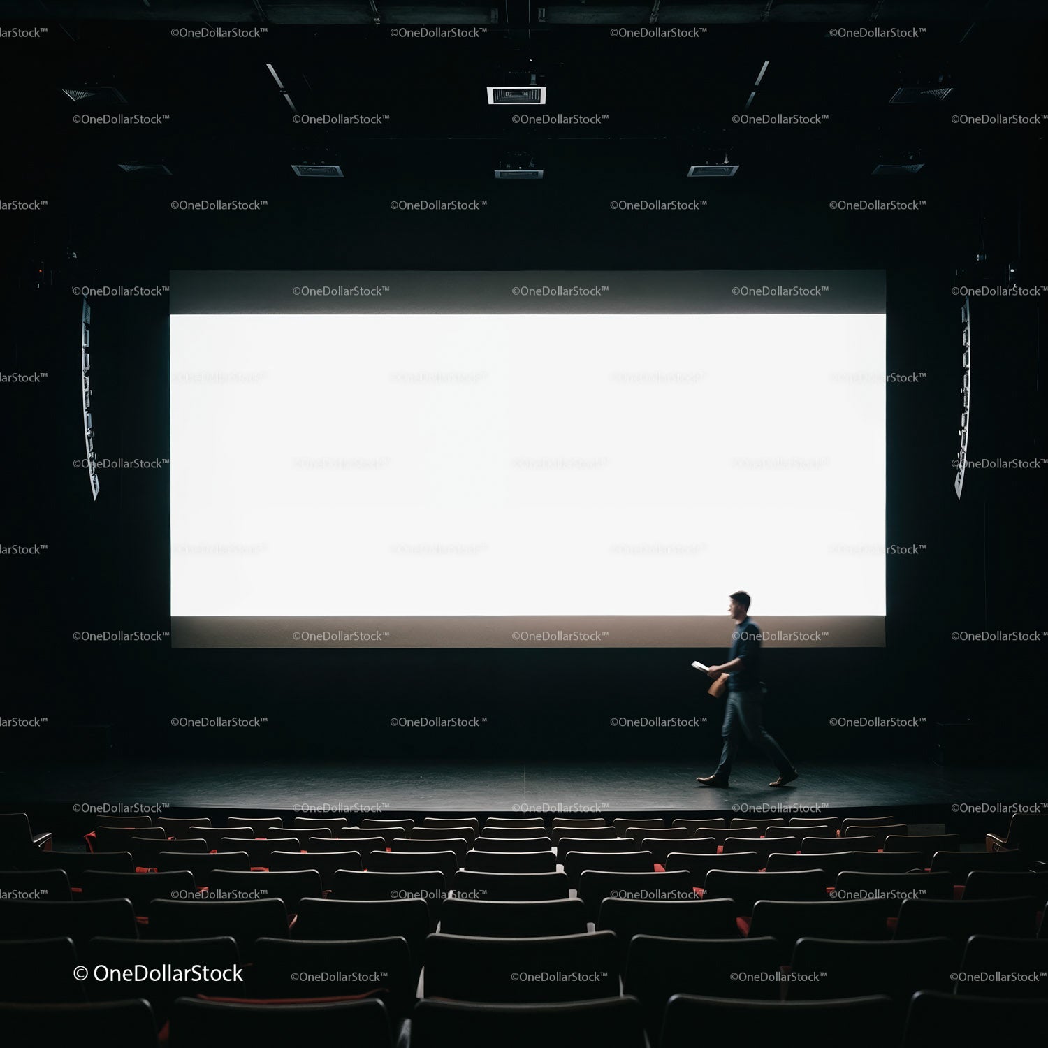 Man Walking Across Dark Theater Stage With Large Screen
