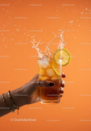 Refreshing iced lemon drink splash in hand on orange background