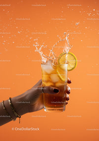 Refreshing iced lemon drink splash in hand on orange background