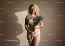 Tattooed Woman Holding Purple Flowers in Lingerie on Minimalist Background