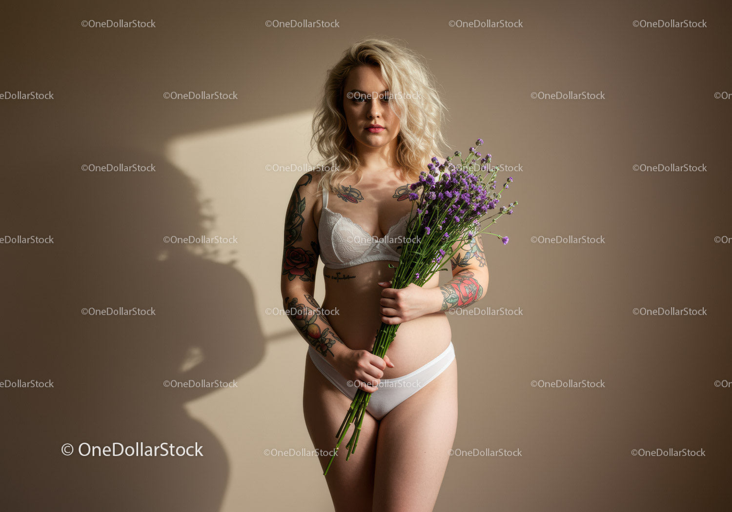 Tattooed Woman Holding Purple Flowers in Lingerie on Minimalist Background