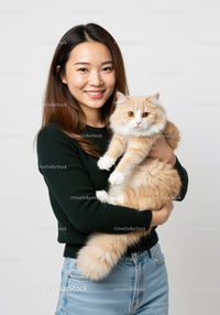 Smiling woman holding fluffy cream cat indoors