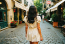 Woman in Cream Dress Walking Along Cobblestone European Street
