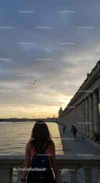 Woman Watching Sunset Over Coastal City Promenade