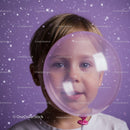 Young child peering through translucent pink balloon with snow