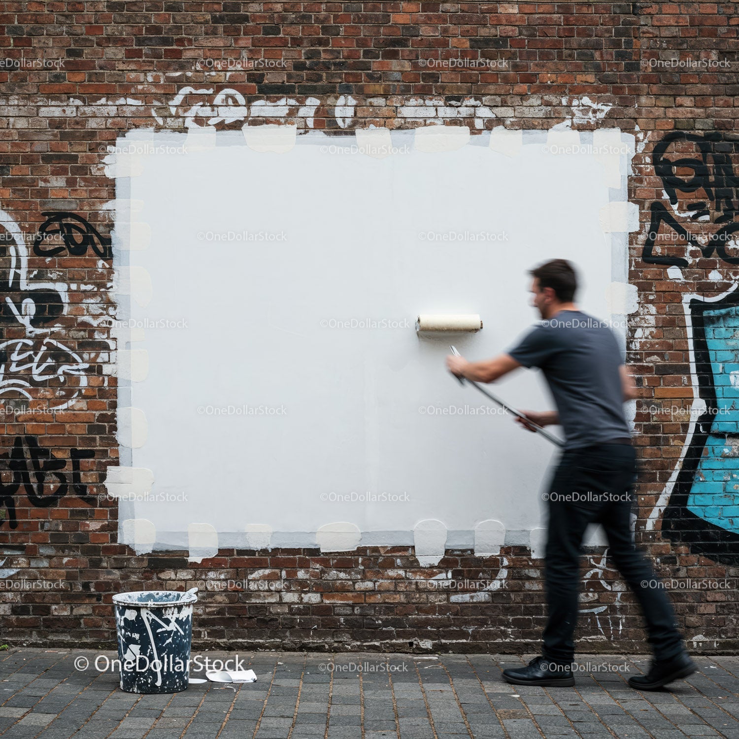 Man painting over graffiti on brick wall with roller