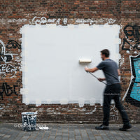 Man painting over graffiti on brick wall with roller
